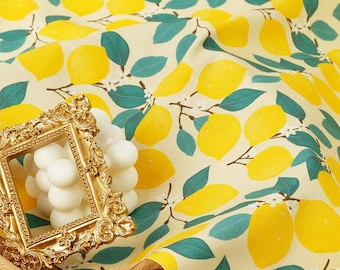 May include: A close-up of a yellow fabric with a lemon print. The fabric is on a woven basket with a gold-colored picture frame on top.