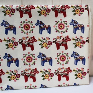 May include: White fabric with a repeating pattern of red and blue stylised horses and floral wreaths. The horses are traditional Swedish Dala horses.
