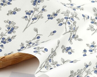 May include: White fabric with a repeating pattern of blue and gray blueberries on branches. The fabric is folded and draped over a wicker basket.