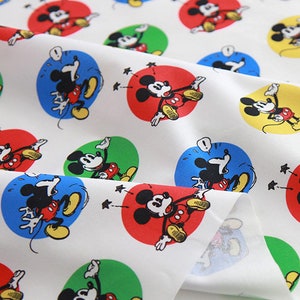 Puede incluir: Tela blanca con un patrón repetido de Mickey Mouse en círculos de diferentes colores. Mickey Mouse está representado en un estilo de dibujos animados con contornos negros y colores rojo, amarillo, azul y verde.