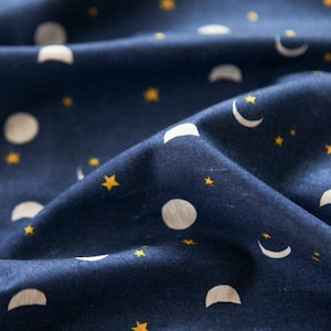 以下が含まれることがあります： 白い三日月と黄色の星が繰り返し描かれた濃い青色の布のアップ画像です。