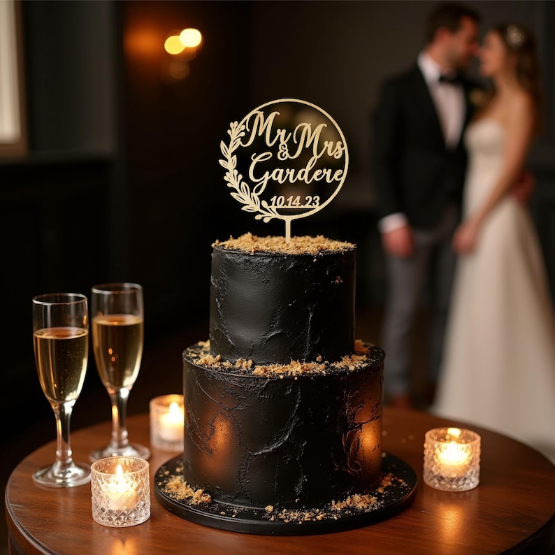 May include: A two-tiered black wedding cake with a wooden topper that reads "Mr & Mrs Gardere 10.14.23". The cake is decorated with a textured frosting and crumbs. Two champagne flutes and lit candles are on the table.