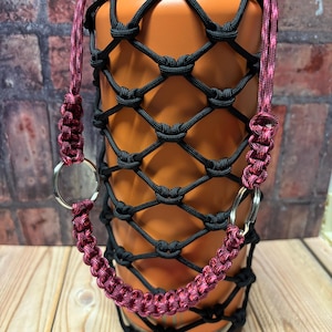 May include: A black and orange water bottle with a black mesh sleeve and a pink paracord handle with silver rings.