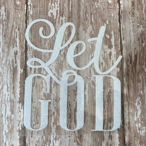 Op de afbeelding: Witte beschilderde letters op een verweerde houten achtergrond lezen "Let God".