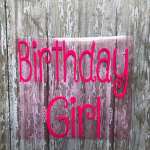 May include: Pink vinyl lettering on a wood background that reads "Birthday Girl".