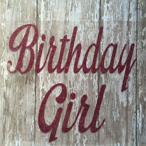 May include: Red glitter vinyl lettering on a wood background that reads "Birthday Girl".