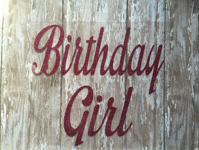 May include: Red glitter vinyl lettering on a wood background that reads "Birthday Girl".