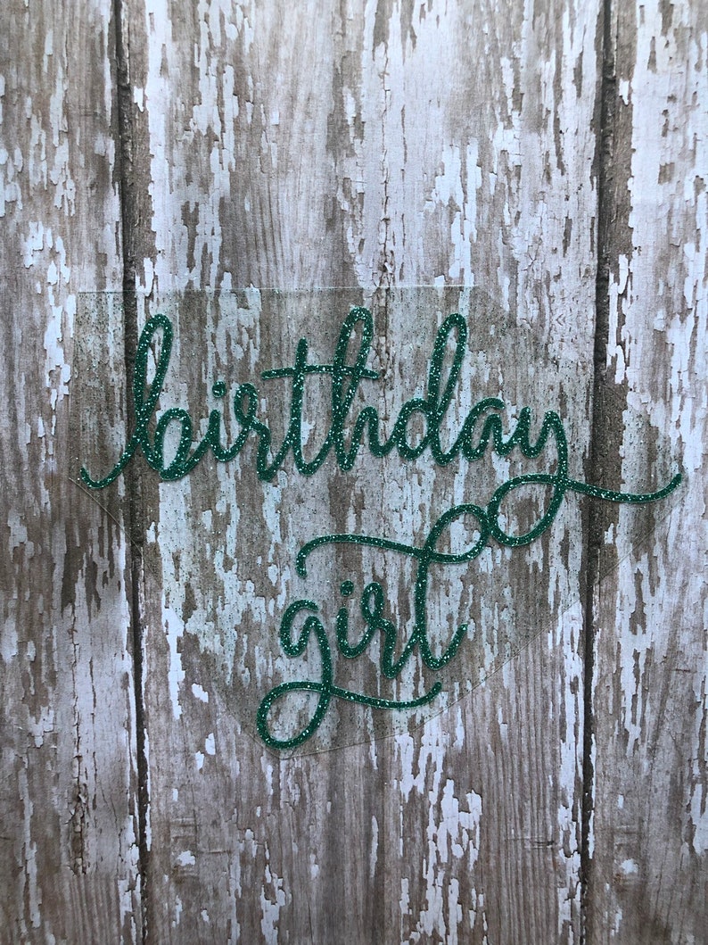 May include: Green glitter birthday girl sign on a wood background.