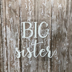 May include: White vinyl lettering on a weathered wood background reads "BIG sister".