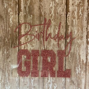May include: A rustic wooden sign with the words "Happy Birthday Girl" in pink glitter lettering.