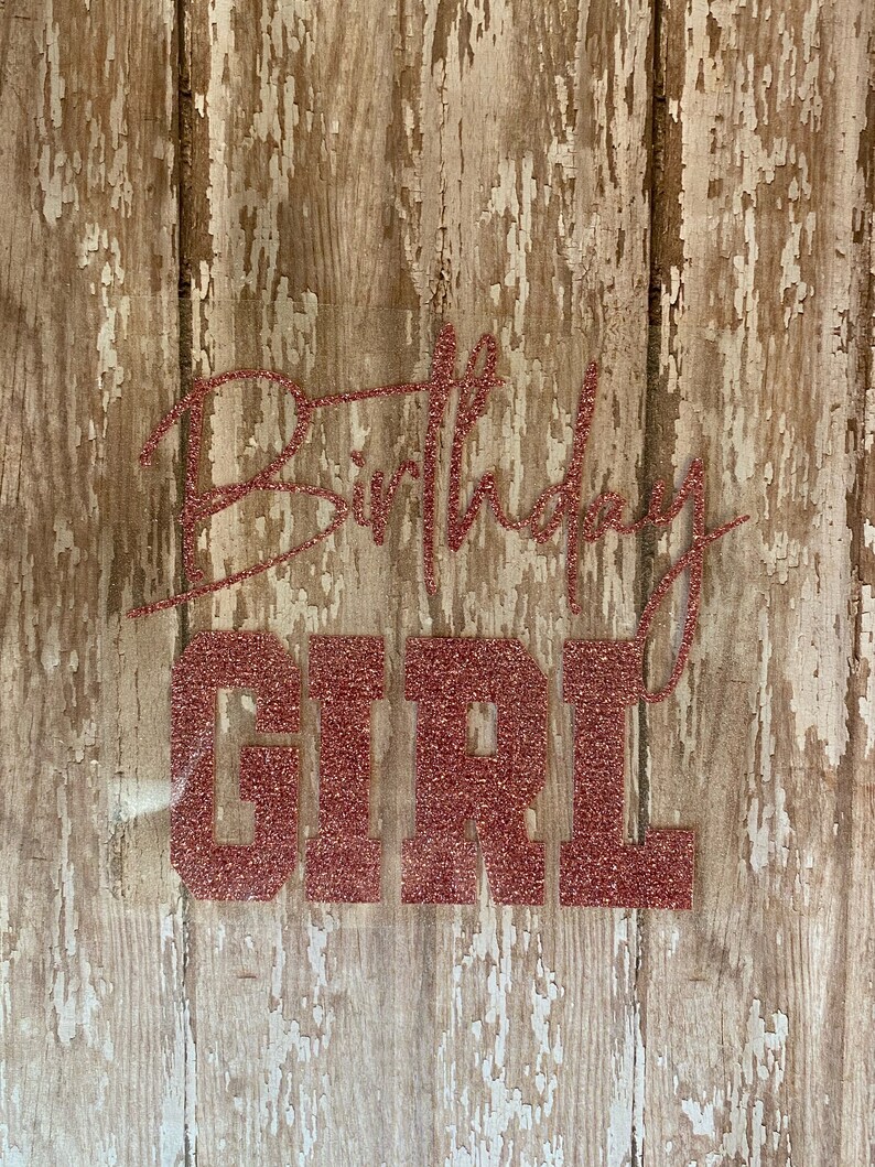 May include: A rustic wooden sign with the words "Happy Birthday Girl" in pink glitter lettering.