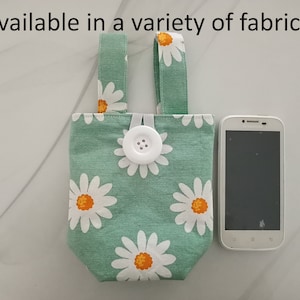 May include: A green fabric phone pouch with a white button and daisy print. The pouch has two straps for carrying.  Available in a variety of fabrics.
