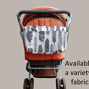 May include: A stroller with a black and white feather print fabric organizer attached to the handle. The stroller is orange and brown with silver wheels. Available in a variety of fabrics.