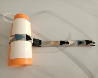May include: A white water bottle with an orange lid and a geometric patterned strap. The strap has a black buckle and a snap closure.