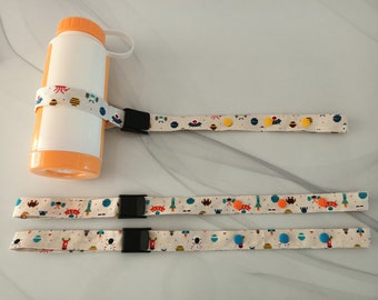 May include: Three beige fabric straps with colorful space-themed patterns and orange, yellow, and blue buttons. The straps have black plastic buckles. A white and orange water bottle is attached to one of the straps.