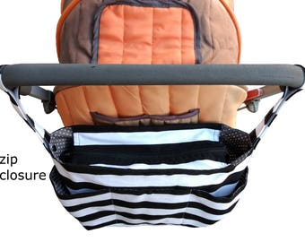 May include: Black and white striped stroller organizer with multiple pockets and a zipper closure. The organizer is attached to the stroller handle.