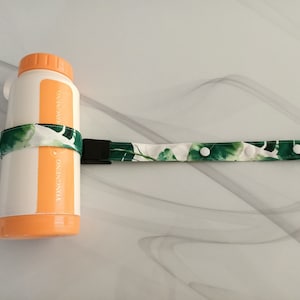 May include: A white water bottle with an orange lid and a green and white patterned strap with white buttons. The strap is attached to the bottle with a black buckle. The bottle has the text "DONGNENG PACKAGING" printed on the side.