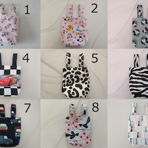 Puede incluir: Nueve bolsas de mano pequeñas con diferentes estampados. Las bolsas tienen dos asas y están hechas de tela. Los estampados incluyen personajes de dibujos animados, estampados de animales y diseños geométricos. Las bolsas son de varios colores, incluyendo rosa, azul y negro.