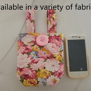 May include: A small pink floral fabric bag with a pink button and a white phone next to it. The bag has two fabric straps and the text "Available in a variety of fabrics" is at the top of the image.