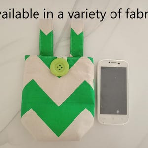 May include: A fabric phone case with a green and white chevron pattern, a green button closure, and green straps. The text "Available in a variety of fabrics" is at the top. A white smartphone is next to the case.