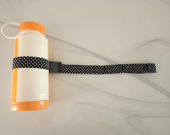 May include: A white water bottle with an orange lid and a black and white polka dot strap. The strap has a black buckle and two black snaps.