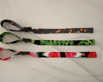 May include: Three fabric wristlets with adjustable closures. The wristlets feature different patterns: gray with orange polka dots, black with green tropical leaves, and black with pink and red watermelon slices.