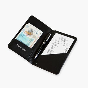 May include: Black leather check presenter with a pen and a receipt. The presenter holds a five-pound note and has the words "Thank you" printed on the inside flap. The receipt lists food items and prices.