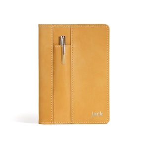 Puede incluir: Una cubierta de cuaderno de cuero amarillo con un portaplumas y el nombre "Jack" grabado en la parte delantera.