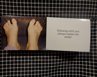May include: A greeting card with a photo of two feet with orange nail polish. The left side of the card has the words "Oh yeah!" and the right side says "Relaxing with you always makes me smile!" The card is on a black and white checkered surface.