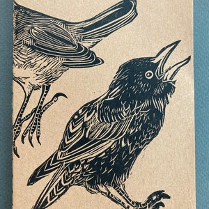 Peut inclure: Gravure sur linoléum en noir et blanc de deux oiseaux. Un oiseau est un corbeau avec son bec ouvert et l'autre est un oiseau plus petit avec ses ailes déployées.