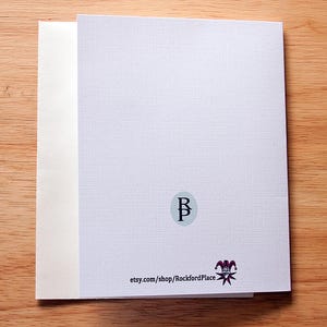 Pu&ograve; includere: Un biglietto bianco con un cerchio blu che contiene la lettera "B" e il testo "etsy.com/shop/RockfordPlace" in nero. Un piccolo grafico di giullare si trova sotto il testo.