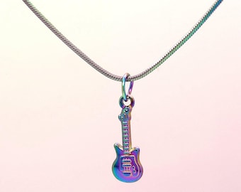 May include: A silver-colored necklace with a guitar pendant. The guitar pendant has a rainbow iridescent finish. The necklace chain is a thin, silver-colored snake chain. The background is a soft, gradient of pink and white.