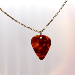May include: A gold chain necklace with a brown tortoiseshell guitar pick pendant.