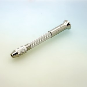 May include: A silver metal hand drill with a knurled handle and a pointed tip.