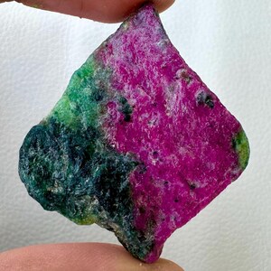 May include: A raw gemstone displaying a vivid colour scheme. The stone showcases a striking blend of deep magenta, emerald green, and dark teal shades. The irregular form and natural texture of the stone are visible.