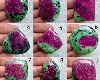 Può includere: Assortimento di nove gemme di rubino zoisite in varie forme. Ogni pietra presenta un vivace centro magenta circondato da zoisite verde e inclusioni nere. Le forme includono tagli ovali, rettangolari e triangolari, mostrando motivi naturali.
