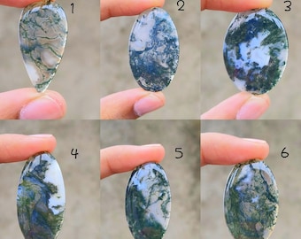 May include: Six polished moss agate gemstones in various oval and teardrop shapes. The stones display a mix of translucent white and green patterns, held up by fingers. Each stone has a unique, natural design.