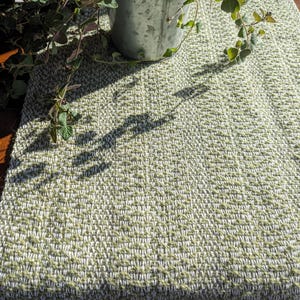 May include: A green and white woven table runner with a textured pattern. The runner is made of natural fibers and has a rustic look.