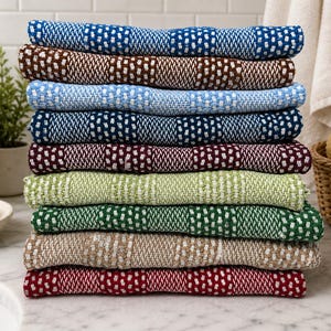 May include: A stack of nine folded rectangular towels featuring a textured weave pattern with alternating blocks of solid color and white. The colors include blue, brown, light blue, dark blue, maroon, lime green, dark green, tan, and red.