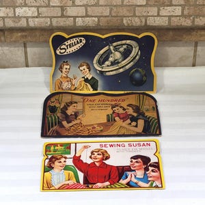 May include: Three vintage sewing needle advertising signs. The top sign features a space station and the word "Stellar". The middle sign reads "One Hundred" and the bottom sign says "Sewing Susan". Each sign has illustrations of women.