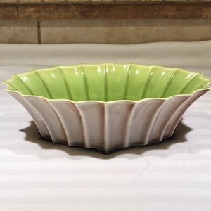 May include: A green and brown ceramic bowl with a scalloped edge. The bowl is shaped like a flower and has a glossy finish.