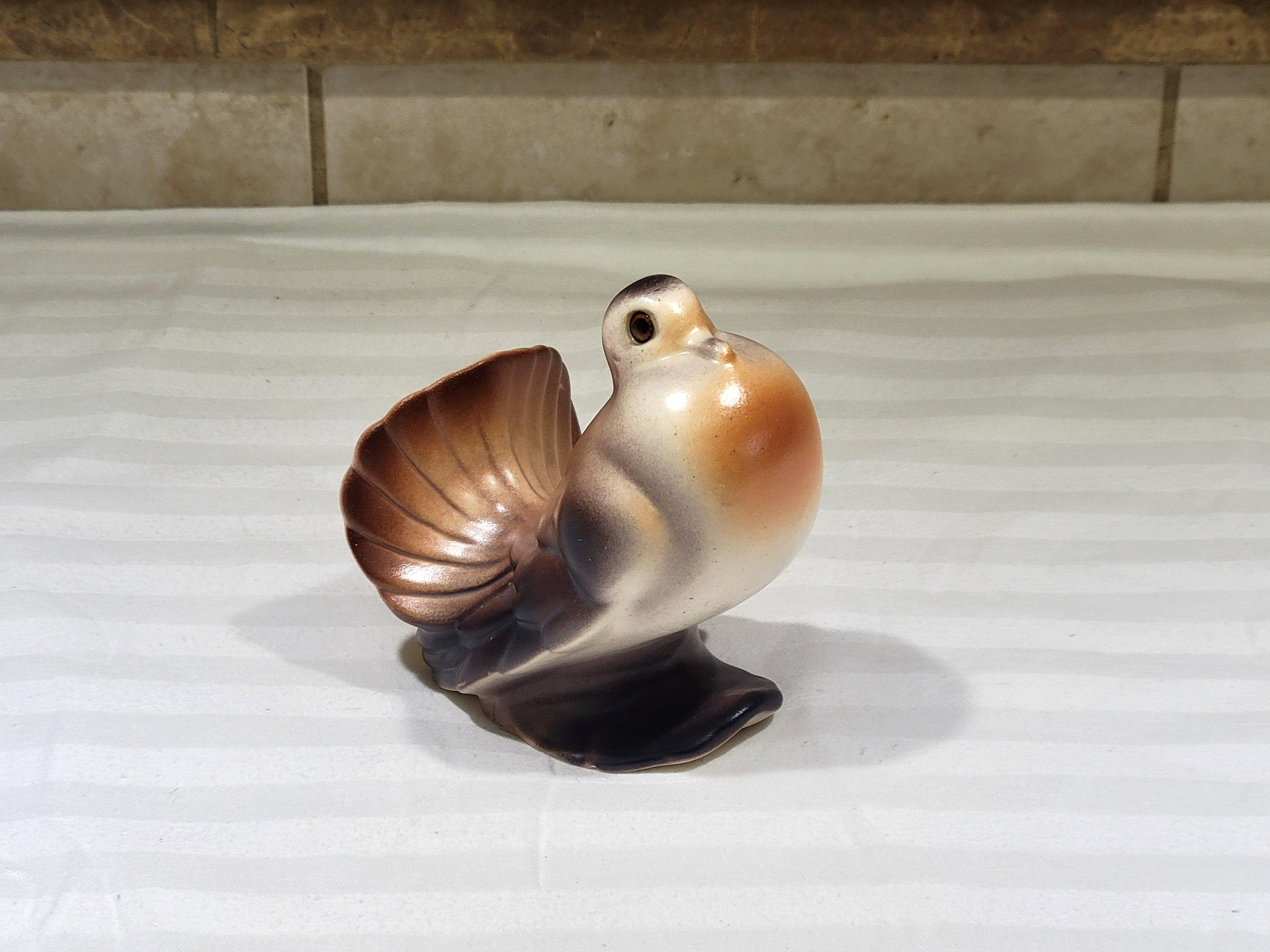 May include: A ceramic dove figurine with a brown, orange, and white color scheme. The bird has a detailed tail and is perched on a dark base. The figurine is likely a decorative item.