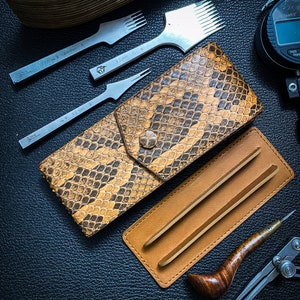 May include: A set of leatherworking tools including a leather punch, a stitching awl, a leather skiver, a pair of tweezers, a compass, and a leather wallet with a snakeskin pattern.
