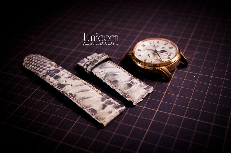 K&ouml;nnte beinhalten: Zwei wei&szlig;e Lederarmb&auml;nder mit einem strukturierten Muster. Die Armb&auml;nder liegen auf einem schwarzen Gitterhintergrund. Der Text "Unicorn handcraft leather" ist oben in der Mitte des Bildes sichtbar.