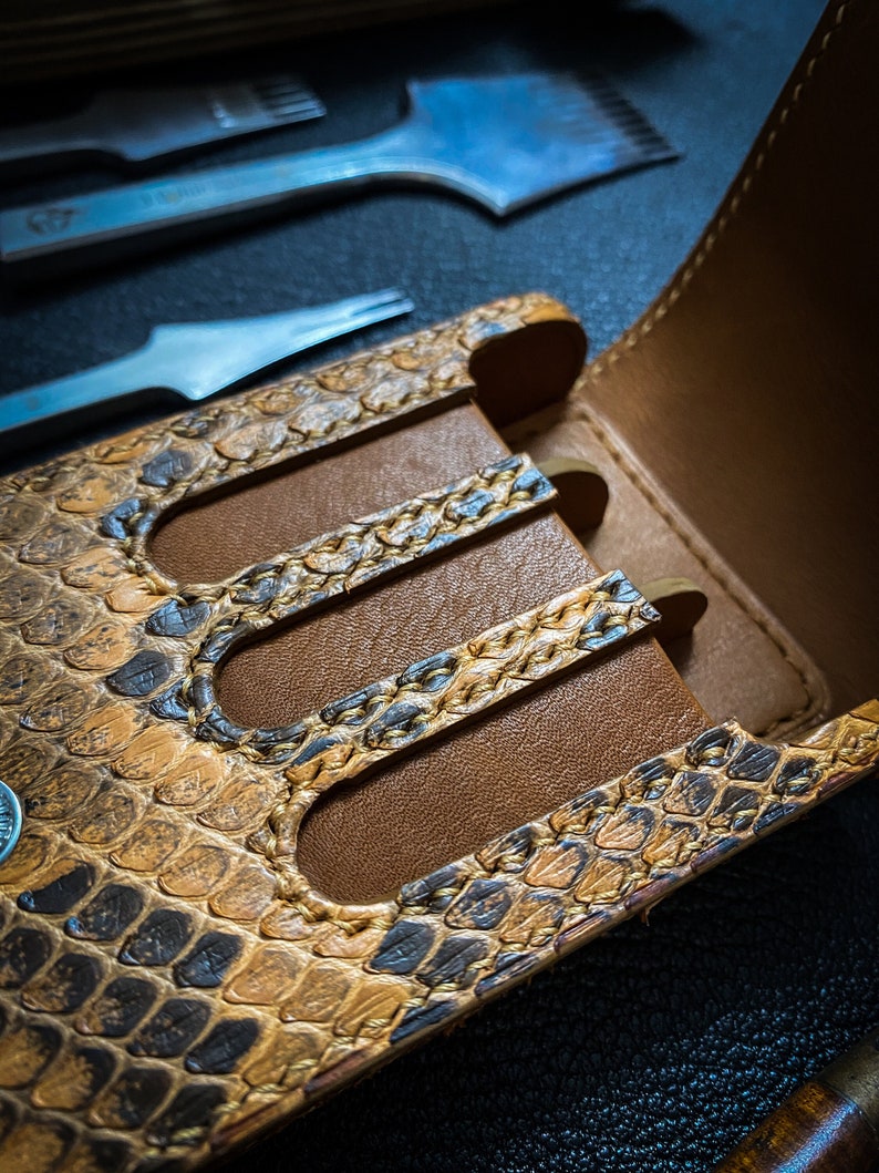 May include: A brown leather case with a snakeskin pattern and three slots for holding tools. The case is open and the slots are empty.
