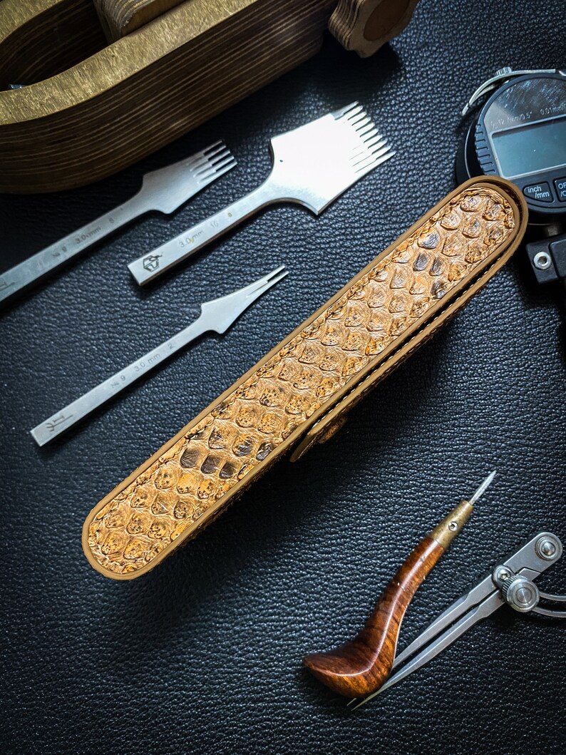 May include: A brown leather case with a snakeskin pattern, a set of leather working tools, a compass, and a digital caliper.