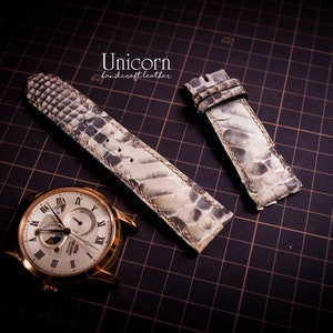 K&ouml;nnte beinhalten: Zwei wei&szlig;e Lederarmb&auml;nder mit Schlangenhautmuster. Die Armb&auml;nder liegen auf einem schwarzen Gitterhintergrund. Der Text "Unicorn handcraft leather" ist oben in der Mitte des Bildes sichtbar.