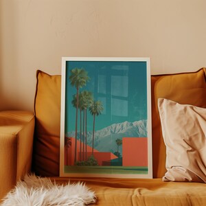 May include: A framed art print featuring a desert landscape with palm trees, red buildings, and mountains under a teal sky. The artwork is displayed on a mustard-colored couch with pillows and a faux fur throw.
