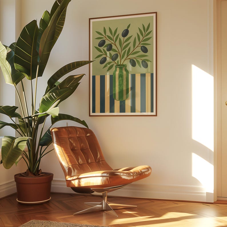 May include: A framed art print featuring a green vase with olive branches and black olives. The background has a green upper section and a striped lower section in blue and yellow. A brown leather chair and a potted plant are in the foreground.