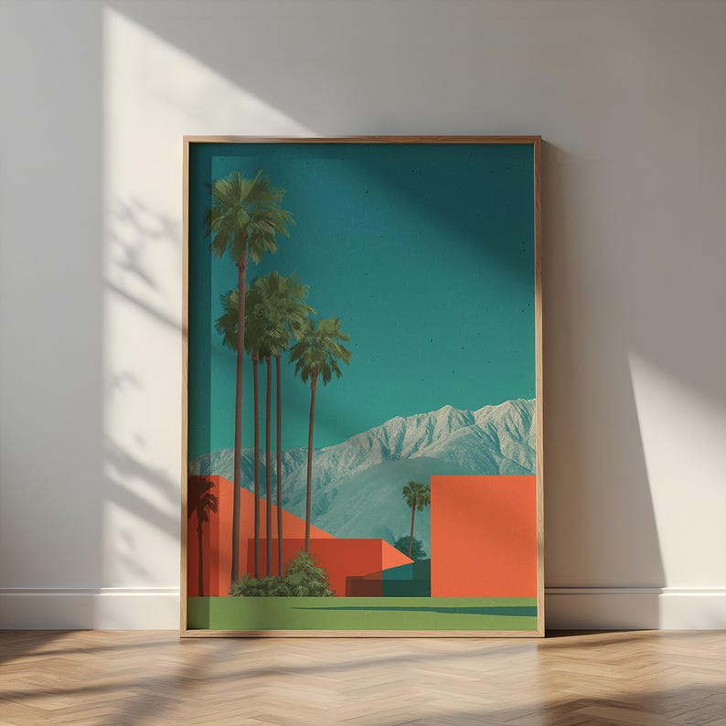 May include: Framed art print featuring a desert landscape with palm trees, orange geometric shapes, and snow-capped mountains under a teal sky. The artwork is displayed in a wooden frame, leaning against a white wall.